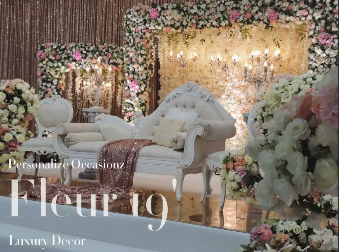 A white carved sofa before blush and peach blooms and gold sequin in the Fleur 19' collection.