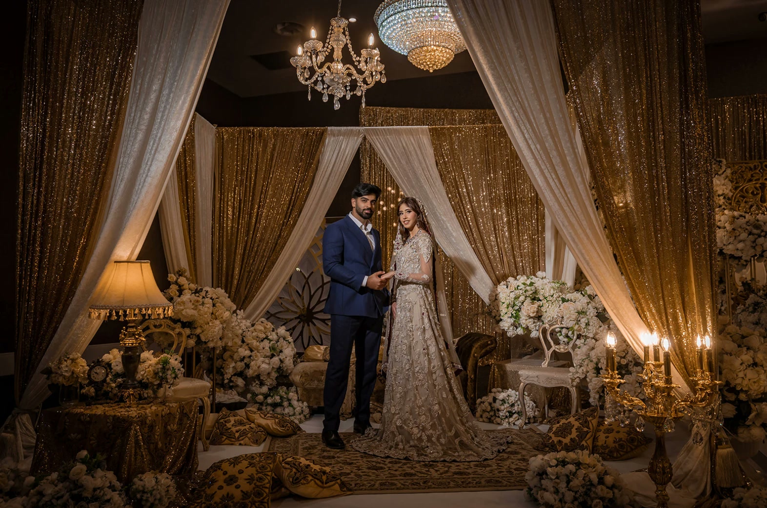 A bride and groom in a stage room of gold sequin and ivory drapes.