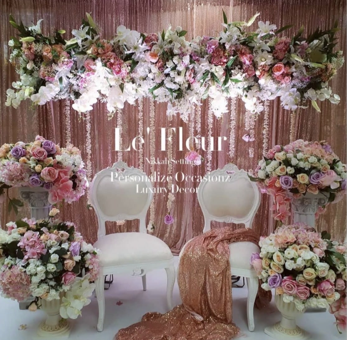 Two white carved chairs among pastel flowers and rose gold drapes in the Le' Fleur nikkah setting.