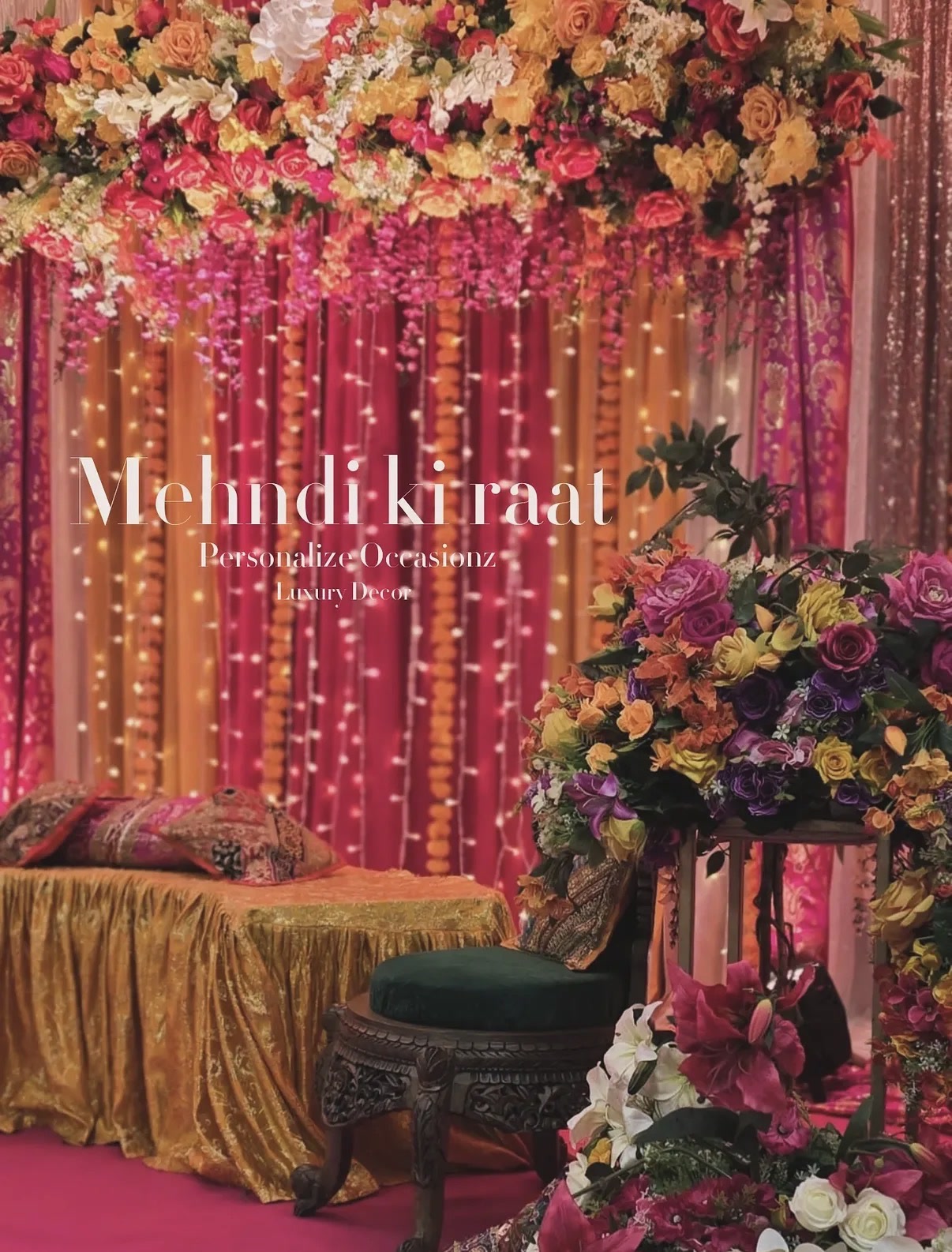 A mehndi stage glowing with fairy lights, pink and marigold drapes and colourful flowers.