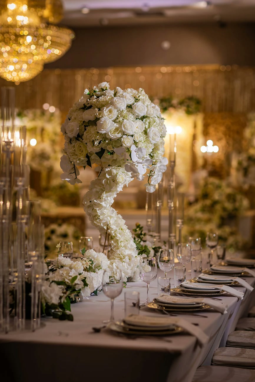 A long table with a tall white orchid and rose centrepiece and candlelight.