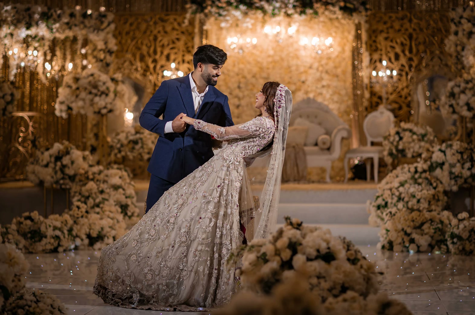 A bride and groom dancing in front of an ivory and gold stage.